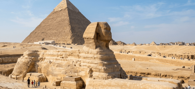 The Great Sphinx statue with the Pyramid of Giza in the background under a clear sky